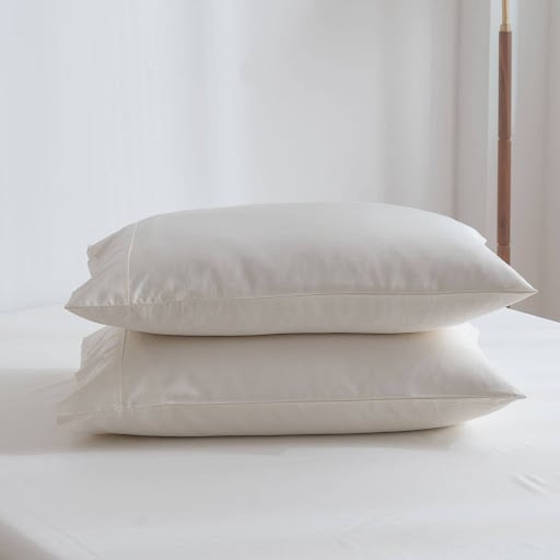 Stack of two white pillows on a neatly made bed, showing smooth and breathable bedding ideal for sensitive skin.
