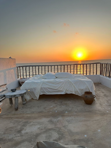 Bed with dermatologist-recommended white sheets set on a terrace overlooking the ocean at sunset, symbolizing restful and skin-friendly sleep.